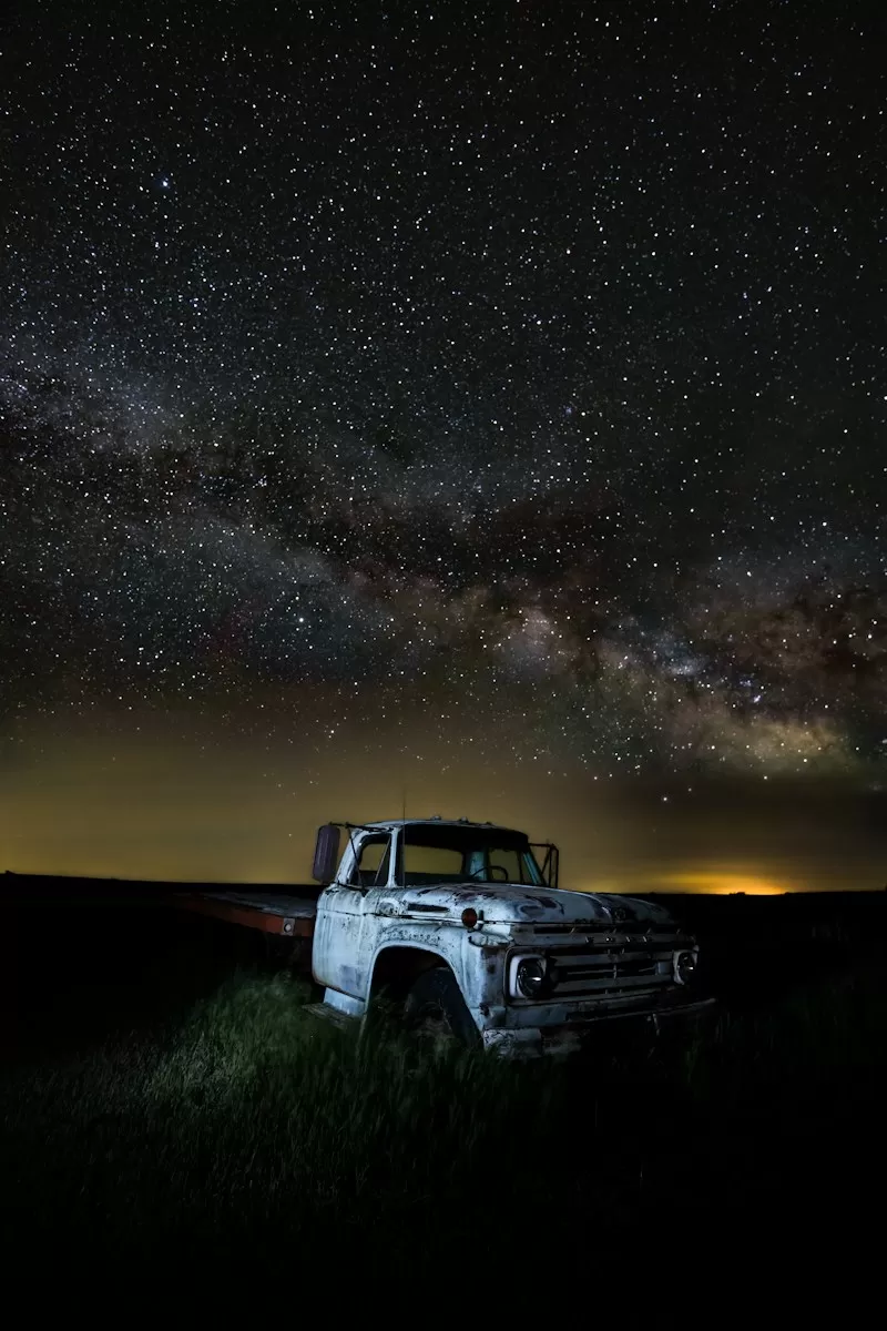 a truck parked in a field under a night sky filled with stars